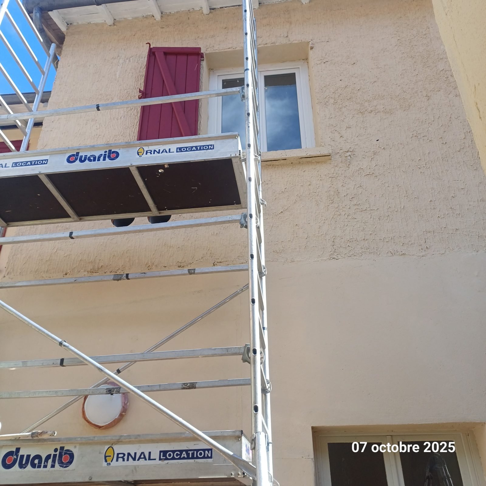 Façade crépie repeinte avec volets bordeaux